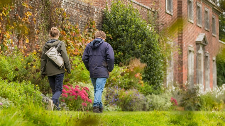Visitors walking along flower border in autumn with exterior of house in background, Uppark, West Sussex